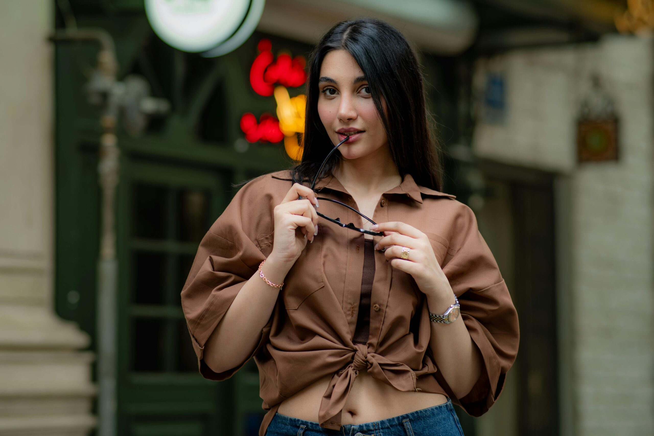 Trendy woman in a brown shirt poses confidently with sunglasses on a street in Tehran, Iran.